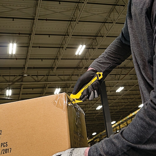 Stanley STHT10356 utility knife cutting box tape in warehouse, close view, person wearing gloves.