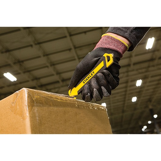 Stanley STHT10360-1 yellow utility knife used to cut cardboard box in warehouse setting.