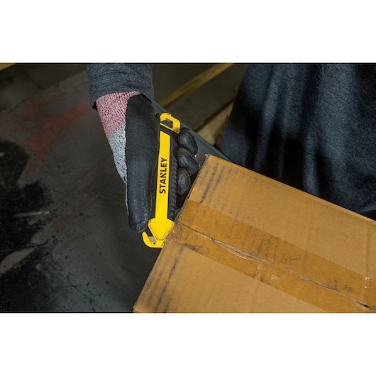 Photo of STANLEY STHT10360-1 utility knife cutting cardboard box, worker wearing black gloves.