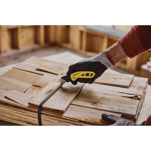 Photo of STANLEY STHT10424 utility knife cutting strapping on stacked wood boards in workshop.