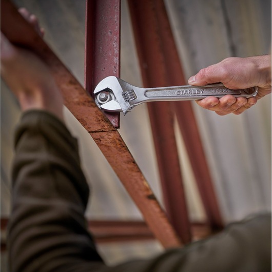 Photography of STANLEY STHT13121-0 adjustable wrench tightening a bolt on a rusted metal beam.