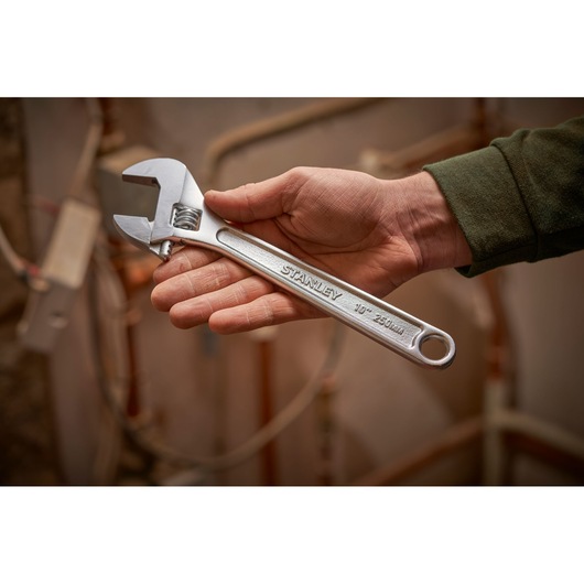 Photo of a STANLEY STHT13121-0 adjustable wrench held in a hand, silver color, used in a workshop setting.
