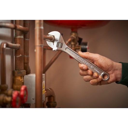 STANLEY STHT13122-0 adjustable wrench used on copper pipes in plumbing setting.