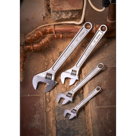 STANLEY STHT13122-0 adjustable wrench set, four sizes, placed on a dusty floor near copper pipes.