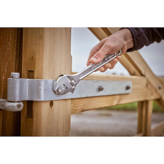 Photo of STANLEY STHT13123-0 adjustable wrench tightening a bolt on a metal hinge attached to a wooden gate.