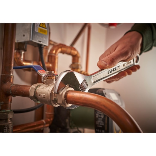Photo of STANLEY STHT13123-0 adjustable wrench used on copper pipe fittings in a plumbing setting.