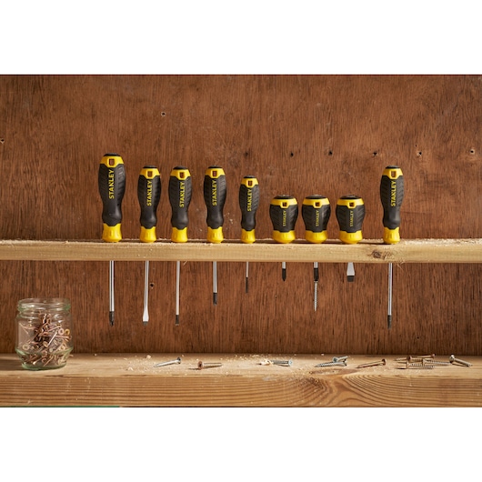 Photo of STANLEY STHT16162-0 screwdriver set, eight black and yellow screwdrivers on wooden shelf with screws.