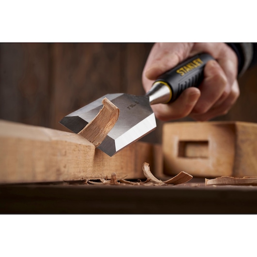 Photo of STANLEY STHT16737-0 chisel with black and yellow handle carving wood, close-up side angle.