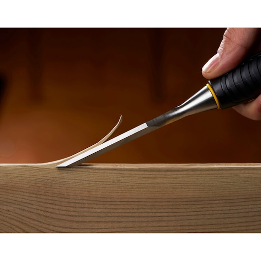 STANLEY STHT16737-0 chisel in use, close-up, carving thin wood shaving from wooden surface.
