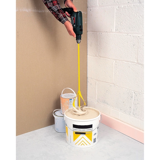 STANLEY STHT2-28043 yellow mixer tool mixing cement in bucket, photographed from above side angle.
