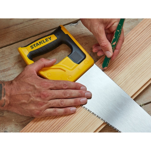 STANLEY STHT20351-1 hand saw with yellow and black handle on wood, close-up during marking process.