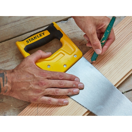 STANLEY STHT20369-1 yellow and black hand saw on wood planks, close-up with hands marking cut line.
