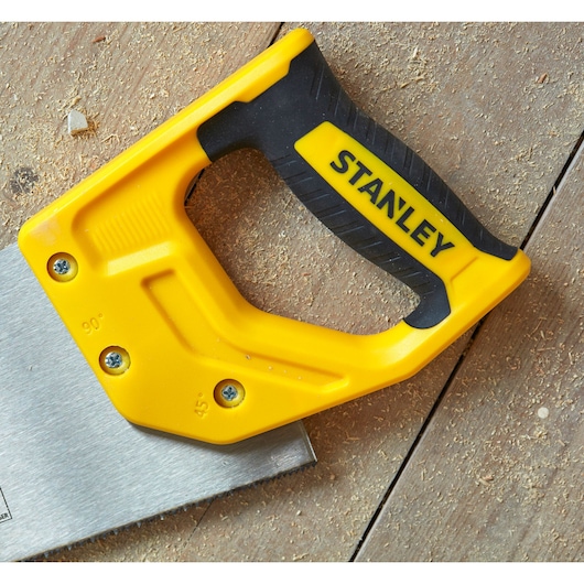 STANLEY STHT20371-1 hand saw with yellow and black handle on wooden surface, close-up angle.