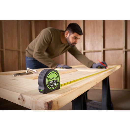 STANLEY STHT30602-1 tape measure on wooden table, person measuring wood, workshop setting.