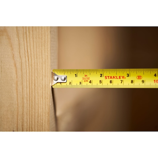 STANLEY STHT30602-1 tape measure measuring wood, close-up of yellow tape with black and red markings.