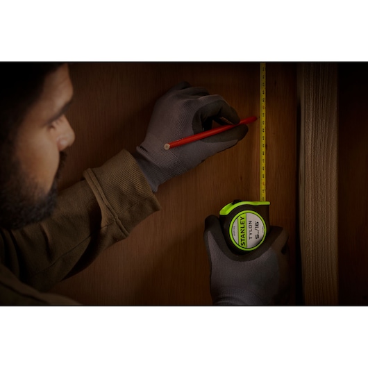 Photography of STANLEY STHT30602-1 tape measure held by a gloved hand against wooden surface.