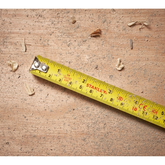 STANLEY STHT30602-1 yellow tape measure on a dusty wood surface, showing centimeter and inch markings.