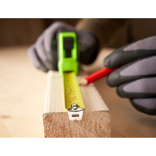 STANLEY STHT30602-1 tape measure on wood, close-up, with gloved hands marking measurements.