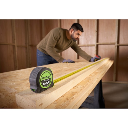STANLEY STHT30604-1 tape measure on wooden workbench, yellow blade extended, person measuring wood.