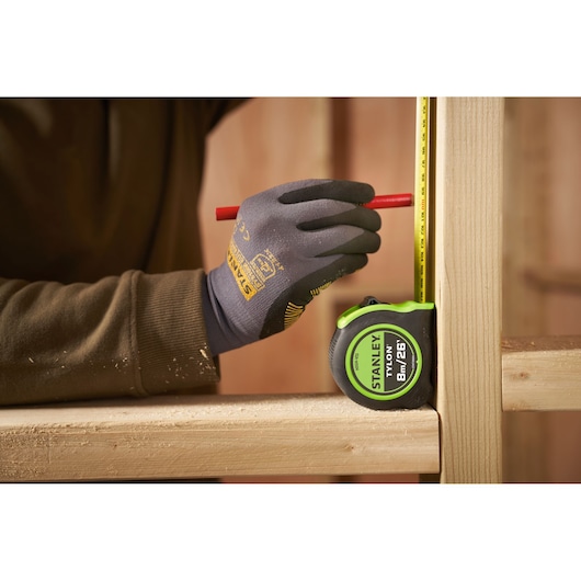 STANLEY STHT30604-1 tape measure held against wood with gloved hand marking measurements, product photography.