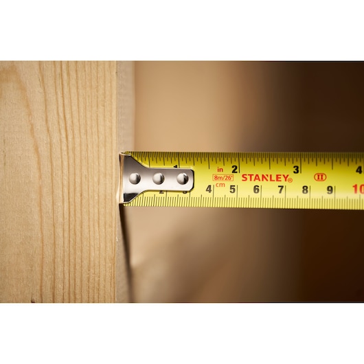 Close-up photo of STANLEY STHT30604-1 tape measure showing yellow blade measuring wood plank.