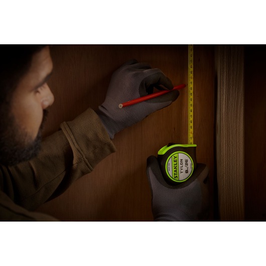 STANLEY STHT30604-1 tape measure held by gloved hand marking wood with pencil, product photography.