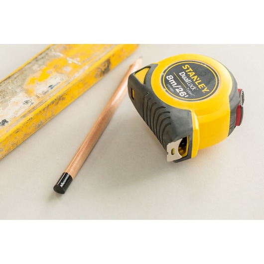 Photo of STANLEY STHT36807-0 tape measure with black-yellow case, pencil, and yellow ruler on a light surface.