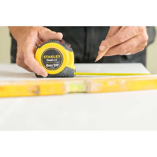 STANLEY STHT36807-0 tape measure held by hand, yellow casing, DualLock, used for marking measurements.