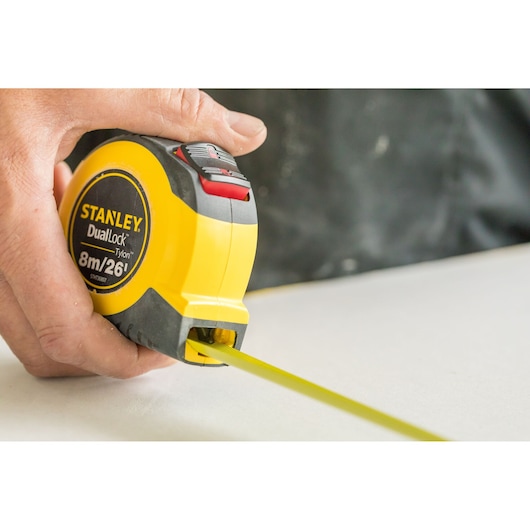 Photo of STANLEY DualLock 8m/26' tape measure, SKU STHT36807-0, being used on a flat surface.