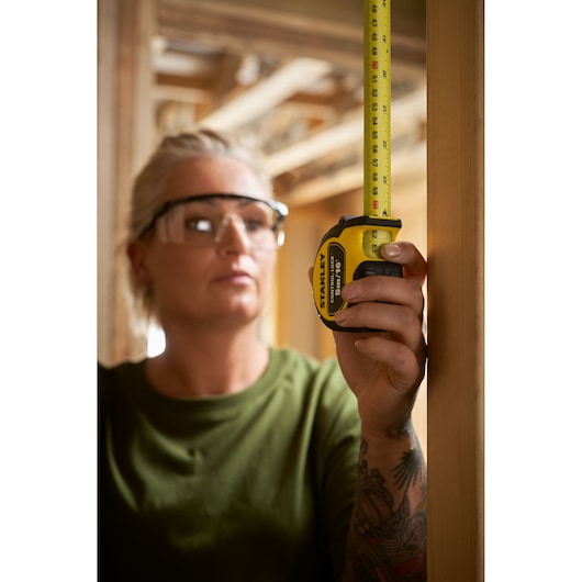 Photo of STANLEY STHT37235 tape measure in use, measuring a wooden beam at a construction site.