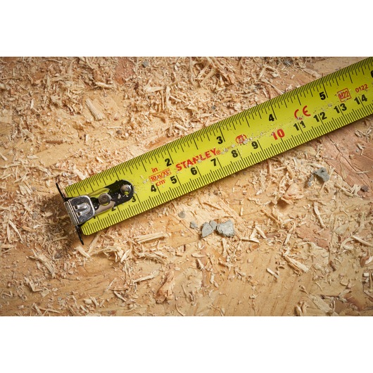 Photo of STANLEY STHT37237 yellow tape measure on a wood surface with sawdust.