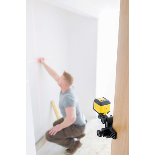 STANLEY STHT77498-1 laser level mounted on a clamp, projecting horizontal and vertical laser lines in a room.
