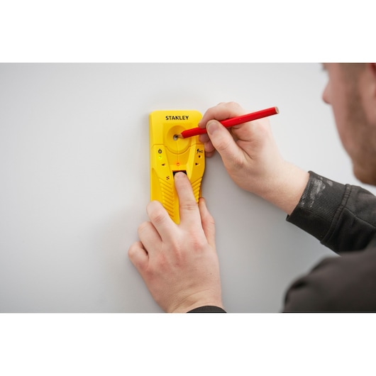 STANLEY STHT77587-0 yellow stud finder held against wall, user marking spot with red pencil.