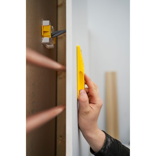 Photo of STANLEY STHT77587-0 wall scanner held against drywall, showing yellow handheld device in use.
