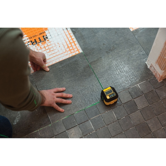STANLEY STHT77592-1 laser level used for tile alignment on a gray tiled floor during installation.