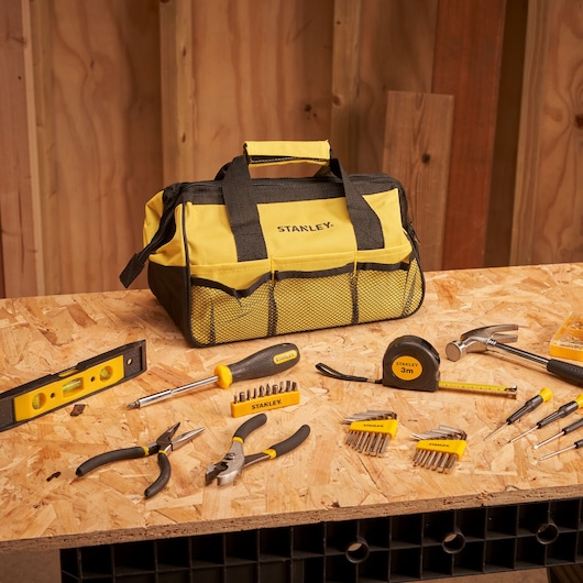 STANLEY STMT0-74101 tool bag with yellow and black tools on a wooden workbench, front angle.