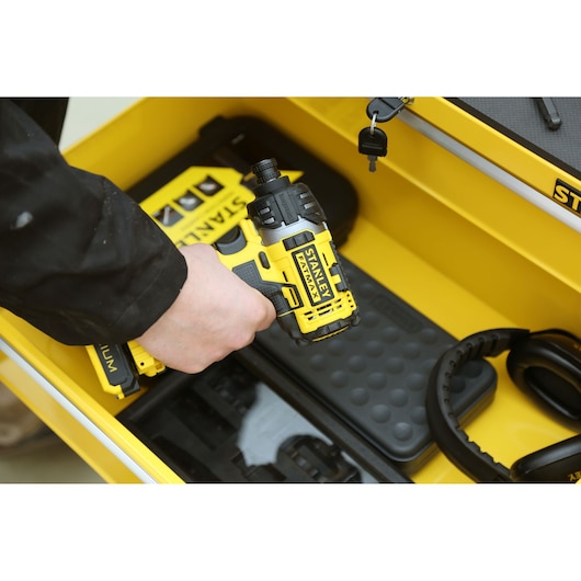 Stanley STMT1-75063 yellow compact impact driver held over tool storage box, side angle.