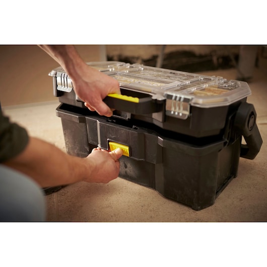 STANLEY STST1-70317 black toolbox with clear lid and yellow handle, shown being opened by hand.