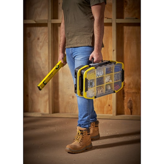 STANLEY STST1-71983 organizer box and spirit level held by person in work boots, workshop setting.