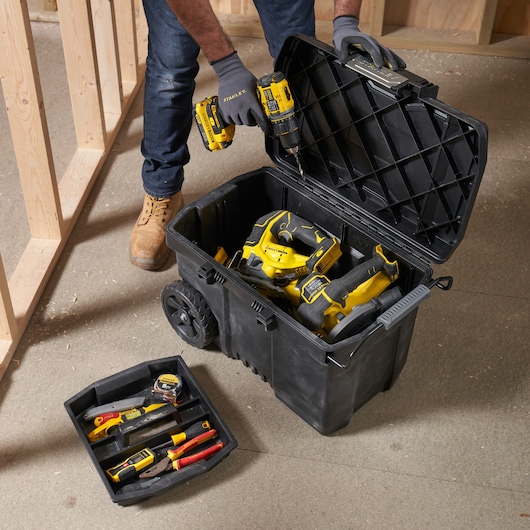 STANLEY STST33090-1 wheeled tool box open with yellow power tools and hand tools inside on construction site.