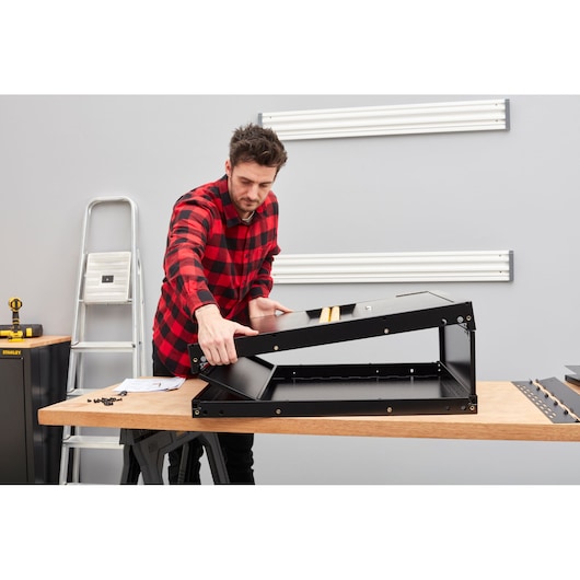 Person assembling a black STANLEY photography accessory on a workbench in a workshop.