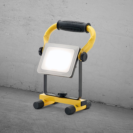 STANLEY SXLS36383E portable LED work light, yellow and black, shown angled in front of concrete wall.