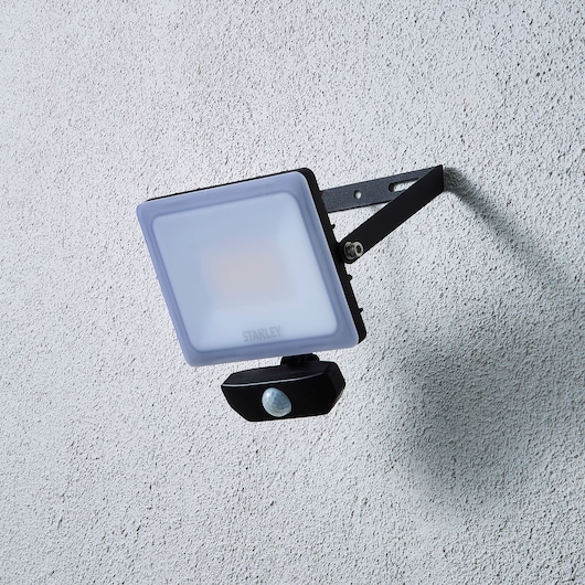 STANLEY SXLS38935E outdoor floodlight with motion sensor mounted on textured wall, side view.