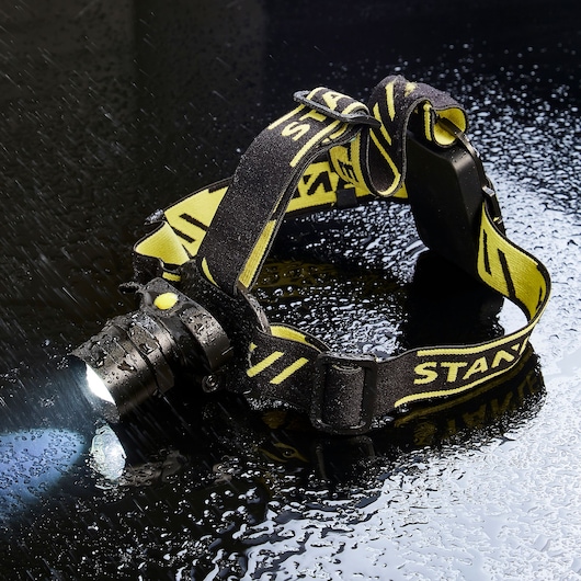 STANLEY SXLS50101E headlamp with yellow and black band, illuminated, on wet surface.