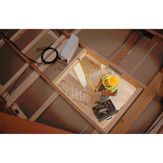 STANLEY XTHT0-33504 tape measure in use by worker in construction setting, viewed from above.