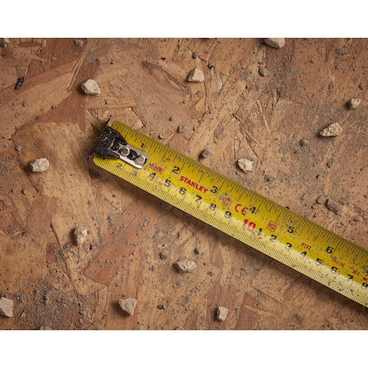 STANLEY XTHT0-33504 yellow tape measure on dusty wooden surface with small rocks, product photography.