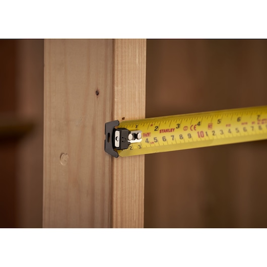 Photo of STANLEY XTHT0-33504 tape measure extended against wooden frame, close-up angle.