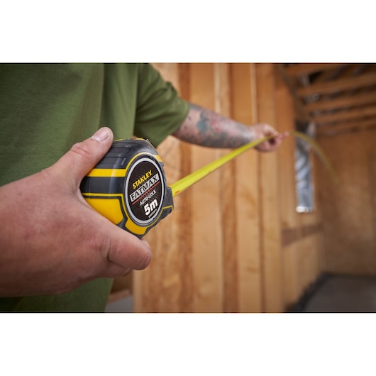 Photo of STANLEY XTHT0-33671 tape measure, black and yellow, being used in a wooden construction interior.
